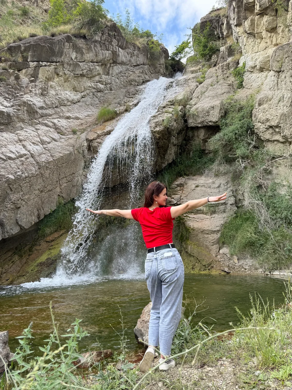 Человек в красной футболке перед небольшим каскадным водопадом и скалами