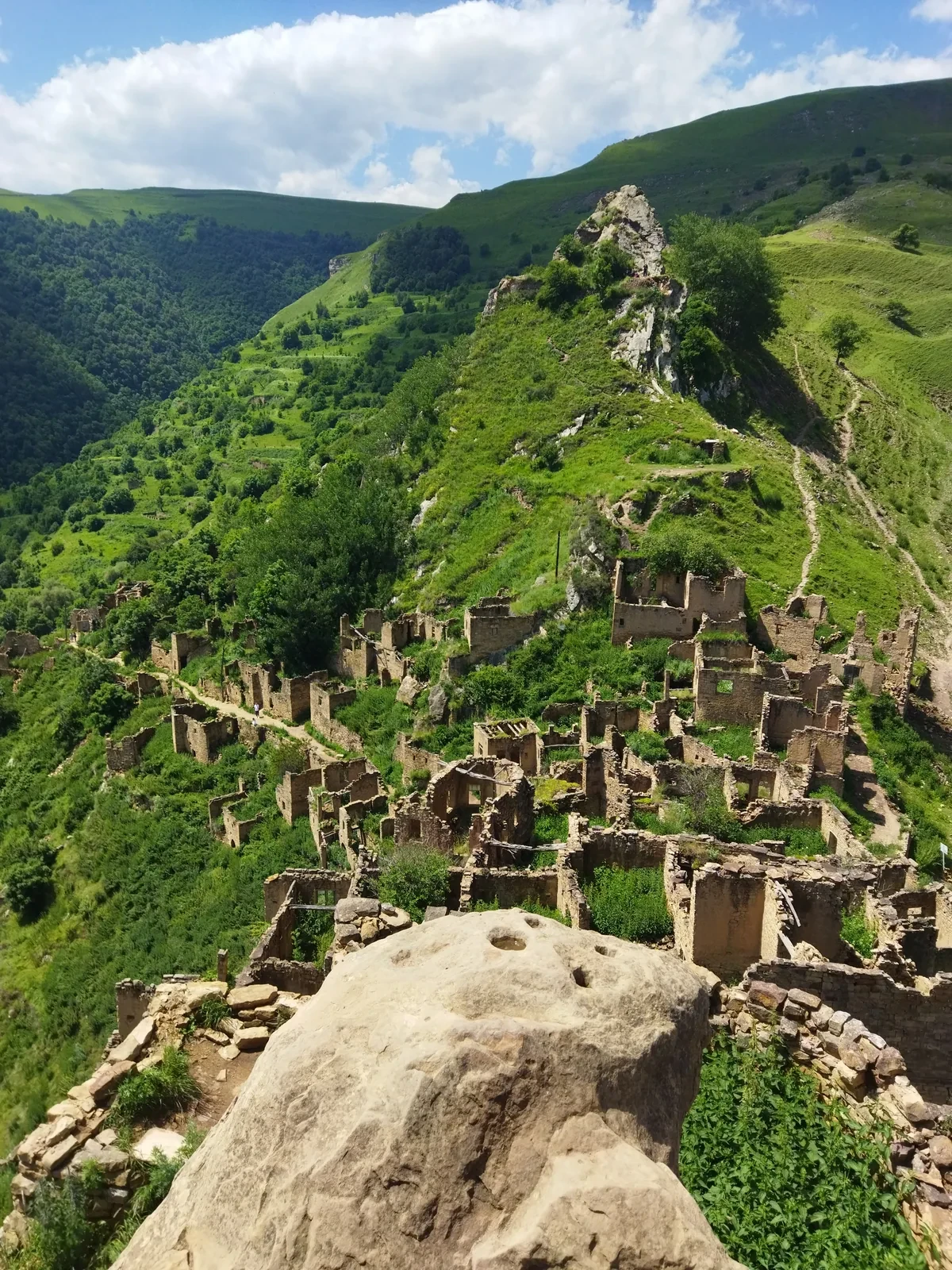 Каменные руины спускаются по узкому зелёному гребню; впереди большой камень