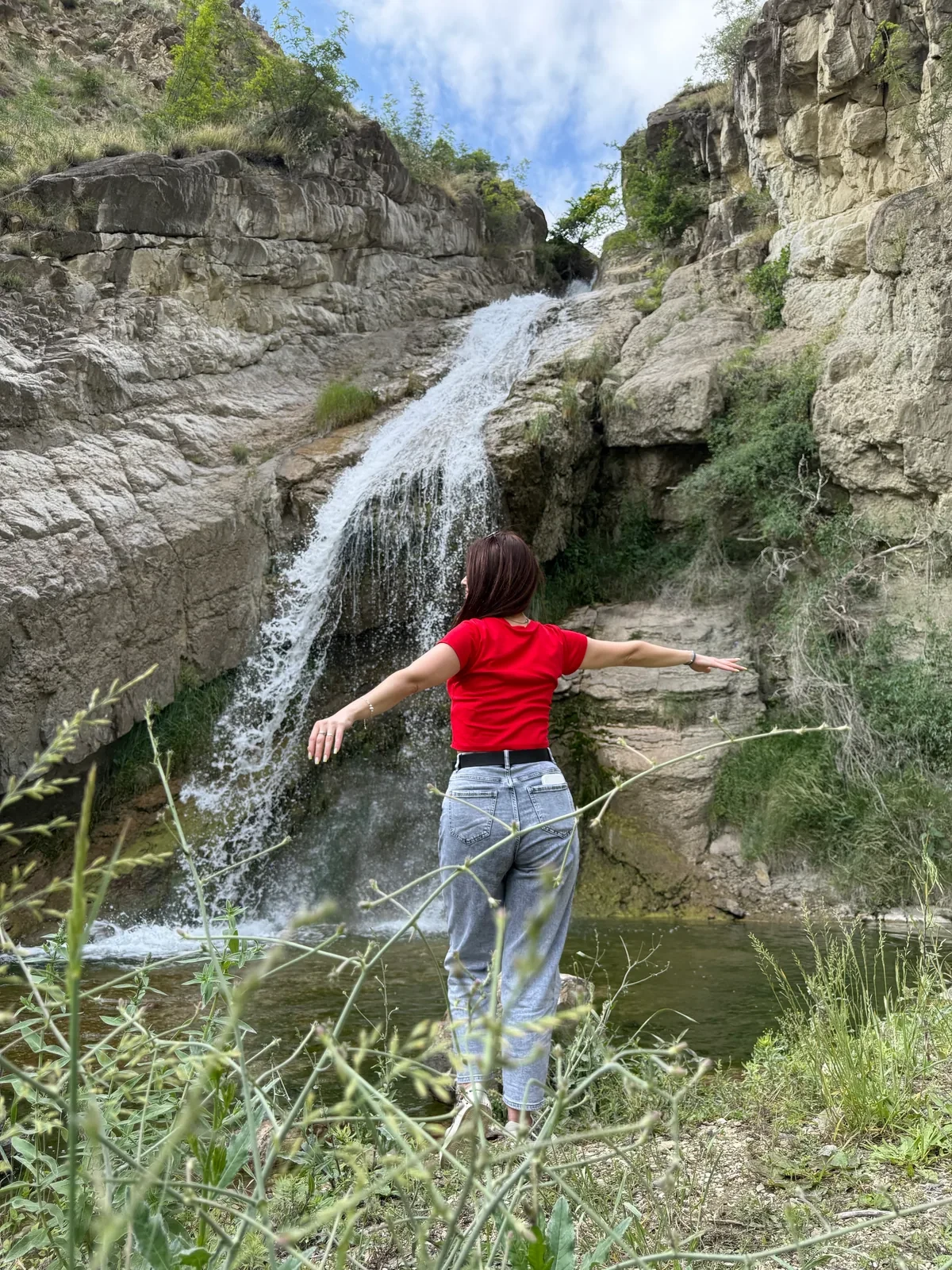 Человек в красной футболке стоит перед каскадным водопадом